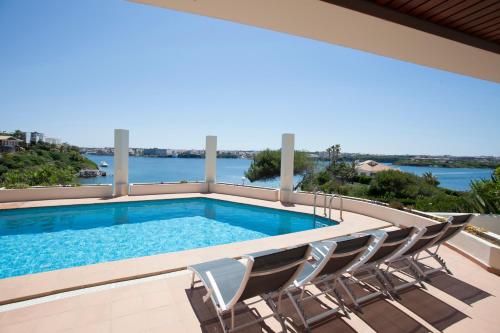 a swimming pool with chairs and a view of the water at VILLA LANTANA Lujo y estilo con vistas únicas al puerto de Mahón in Cala Llonga