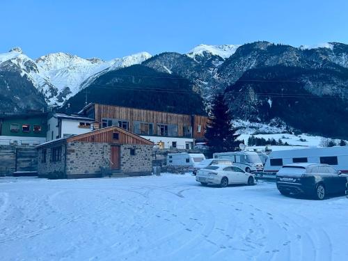 a building with cars parked in a parking lot with snow covered mountains at ArlBerglife Ferienresort in Pettneu am Arlberg