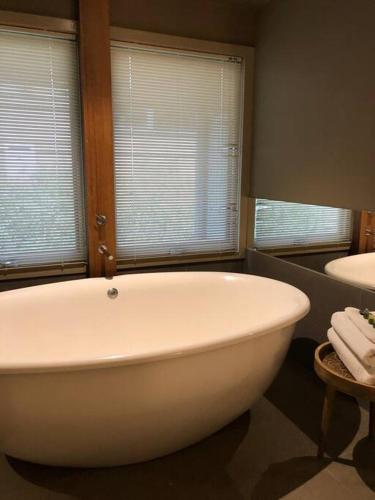 a white bath tub in a bathroom with two windows at Hepburn Hideaway Villa ~ Hepburn / Daylesford in Hepburn Springs