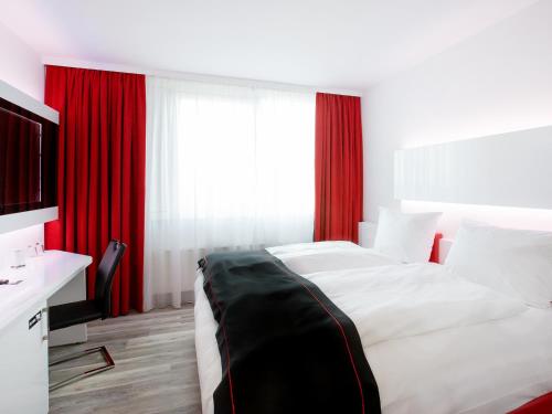 sypialnia z dużym łóżkiem z czerwonymi zasłonami w obiekcie DORMERO Hotel Hannover-Langenhagen Airport w Hanowerze
