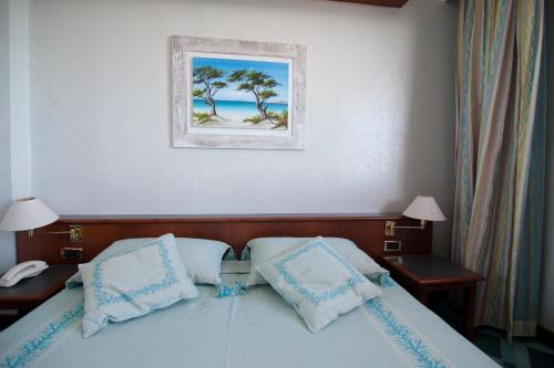 a bed with two pillows and a picture on the wall at Club Esse Roccaruja in Stintino