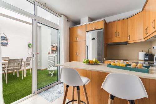 una cocina con armarios de madera y sillas blancas y un comedor. en Home2Book El Perenquén Las Canteras, en Las Palmas de Gran Canaria