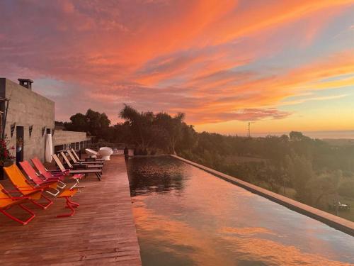 a pool with chairs and a sunset in the background at Kohinor maison d'hôtes in Douar Oulad ben Kheja