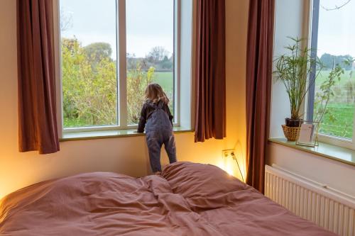 une petite fille debout au-dessus d'un lit donnant par la fenêtre dans l'établissement Huisje op Bioboerderij, kust, polder en rust, à Hoofdplaat