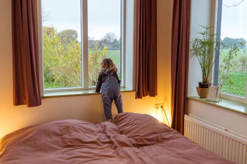 a little girl standing on top of a bed looking out the window at Huisje op Bioboerderij, kust, polder en rust in Hoofdplaat