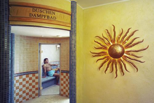 a man in a bathroom with a painting of a sun on the wall at Rüters Parkhotel in Willingen
