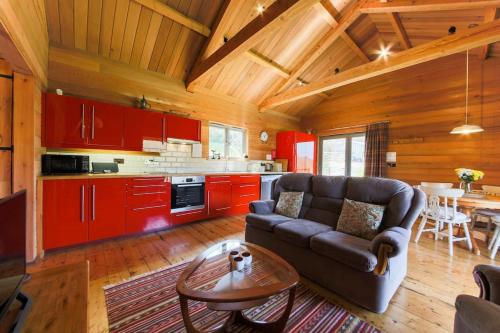 un salon avec un canapé et une cuisine avec des placards rouges dans l'établissement Kingfisher Cabin, Butterwell Farm, Riverside cabin on 40-acre private estate, à Bodmin