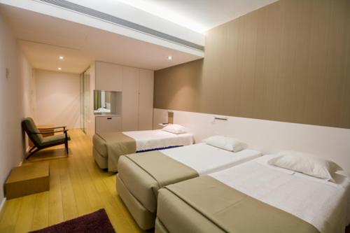 a hotel room with two beds and a chair at Hotel Laranjeira in Viana do Castelo
