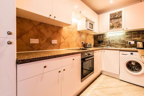 a kitchen with white cabinets and a washer and dryer at Comfy Apartment 16 Easy access to Central London in Tadworth