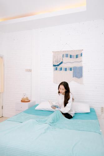 a woman sitting on a bed reading a book at Roemah Renjana Yogyakarta in Timuran