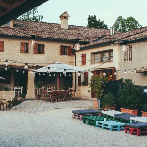 an outdoor patio with tables and umbrellas in front of a building at Asolo Norah's Hill Agri Rooms in Caenere