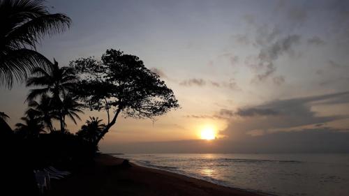 a sunset on a beach with palm trees and the ocean at CASE de ROBINSON in Lomé