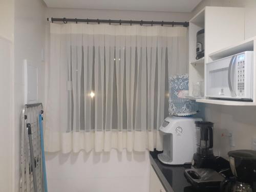 a kitchen with a window with white curtains and a microwave at Lençóis Confort Barreirinhas in Barreirinhas