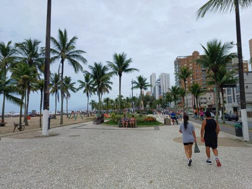 twee mensen lopen over een strand met palmbomen bij Praia Grande Boqueirão e Guilhermina in Praia Grande