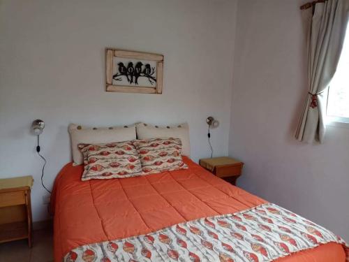 a bedroom with a bed with an orange and white comforter at Cabañas Rincon Verde in Merlo