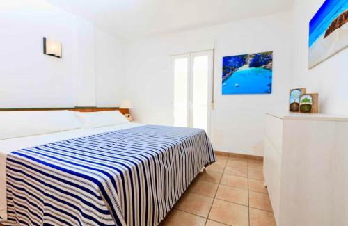 una camera con un letto con una coperta a righe blu e bianche di APARTAMENTO SA VARADERO 2D VISTA MARE LATERALE a Es Pujols
