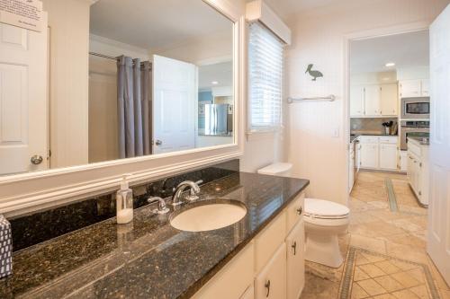 een badkamer met een wastafel, een toilet en een spiegel bij Anchored In in Kure Beach