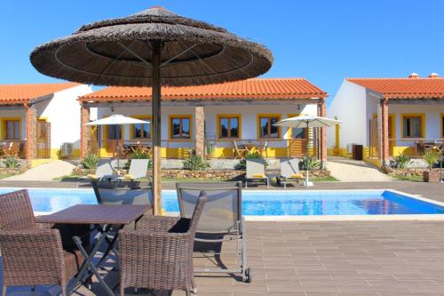 a table and chairs with an umbrella next to a pool at Quinta das Alfambras in Aljezur