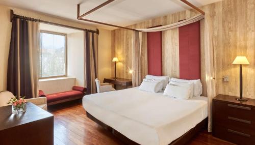 a hotel room with a large white bed and a chair at NH Collection Palacio de Burgos in Burgos