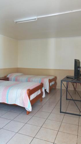 Habitación con 2 camas, TV y mesa. en Hostal Amunategui, en La Serena
