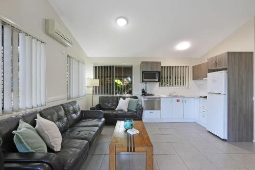 a living room with a black leather couch and a kitchen at Reflections Moonee Beach - Holiday Park in Moonee Beach