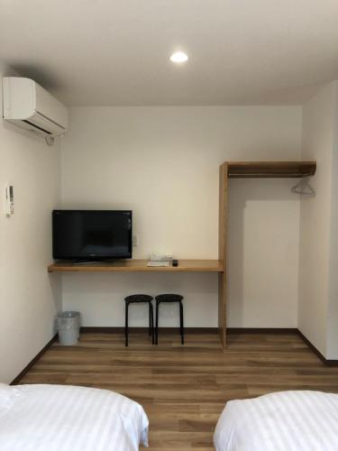 a room with two beds and a tv on a wall at Minshuku Cress in Biei