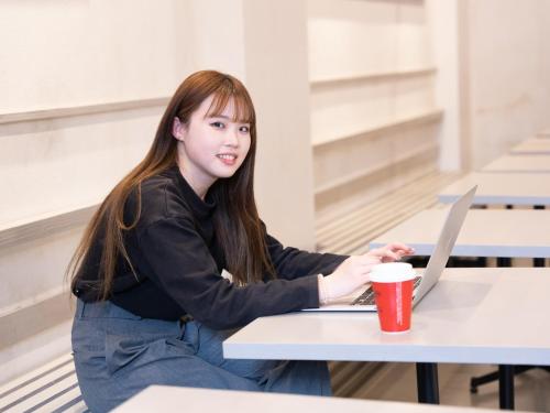 a young girl sitting at a table with a laptop at Hiromas Hostel Yokohama Chinatown in Yokohama