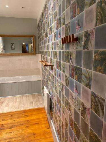 a bathroom with a tile wall with a tub and a mirror at Le Bois derre gite in Éancé
