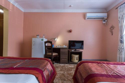 a room with two beds and a desk and a refrigerator at Comfort Gardens in Nairobi