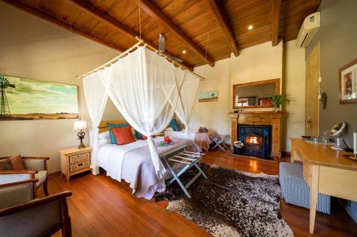 a bedroom with a canopy bed and a fireplace at De Zeekoe Guest Farm in Oudtshoorn