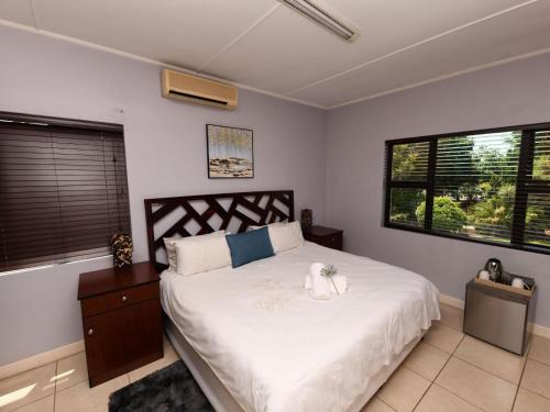 a bedroom with a large bed with white sheets and windows at Blue Sands Guest House in Pietermaritzburg