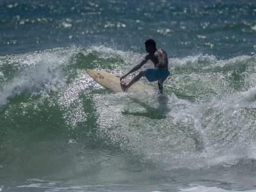 un homme chevauchant une vague sur une planche de surf dans l'océan dans l'établissement Beach front Cottage, à Mahambo