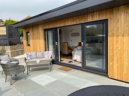 a patio with a sliding glass door with a couch and chairs at Spacious Studio Cabin with Sea/ Downs views Sole Use of HotTub in Seaford in Seaford