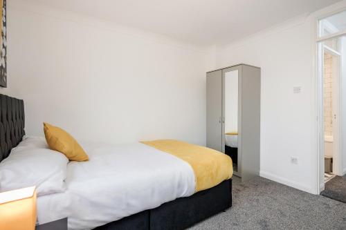 a bedroom with a bed with white sheets and yellow blanket at Lovely House in Dagenham / Barking with free parking, WiFi & Garden in Dagenham