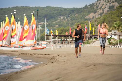 two people walking on the beach with sailboats at ROBINSON SARIGERME PARK - All Inclusive in Dalaman