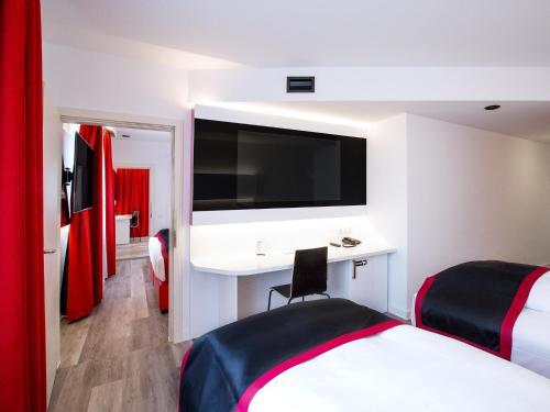 ブルクハウゼンにあるDORMERO Hotel Burghausenのベッド、デスク、テレビが備わるホテルルームです。