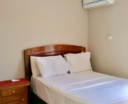 a bedroom with a bed with white sheets and a wooden headboard at Summer Grove Villa in Kololi