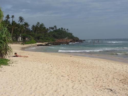 a person laying on a beach next to the ocean at Mallis Guesthouse in Habaraduwa