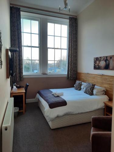 a bedroom with a bed and two windows at Grammar Lodge Guest House in Campbeltown