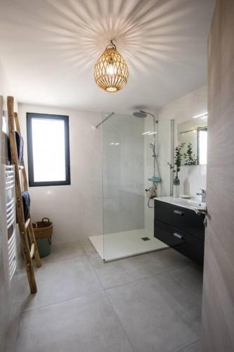 La salle de bains est pourvue d'une douche, d'un lavabo et d'un lustre. dans l'établissement Stanatura Appt 2 chambres vue panoramique #INDENO, à Porto-Vecchio