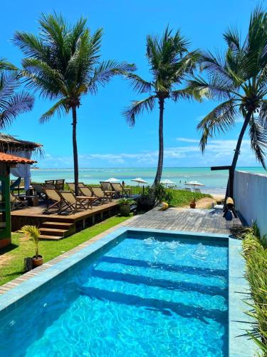 a pool with palm trees and the ocean in the background at Pousada Rota Ecológica in Pôrto de Pedras