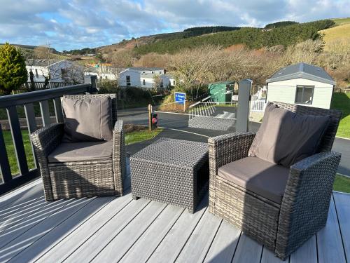 two wicker chairs and a table on a deck at Mawgan Pads Lazy Days Lodge in Mawgan Porth