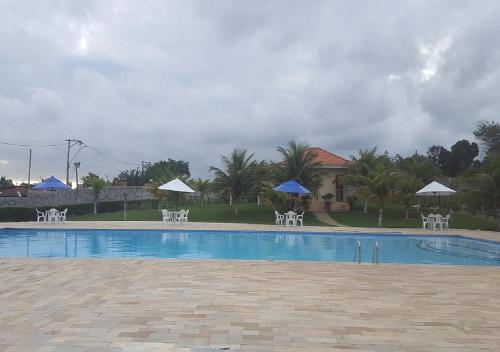 a swimming pool with white chairs and umbrellas at Recanto de Araruama in Araruama