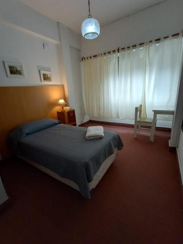 a bedroom with a bed and a chair and a window at Hotel Iberia in Neuquén