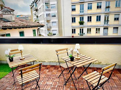 3 tables et chaises en bois sur une terrasse avec des bâtiments dans l'établissement Alkecè White, à Udine