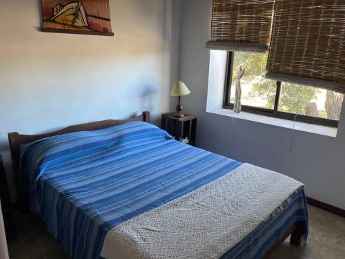 1 dormitorio con 1 cama con edredón azul y ventana en La Pasionaria casa cerca del mar, en Punta del Diablo