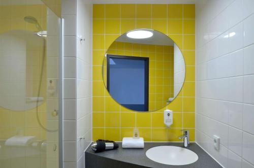 Baño de azulejos amarillos con lavabo y espejo en B&B Hotel München City-Ost en Múnich