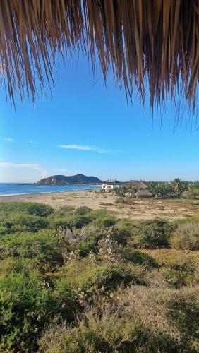 a view of a beach with the ocean and a straw roof at Casa Gitana in Chamuscadero
