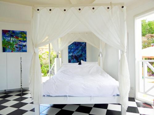 ein Schlafzimmer mit einem weißen Himmelbett und einem karierten Boden in der Unterkunft TOUDOU DOUDOU in Deshaies
