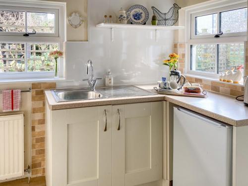 a kitchen with white cabinets and a sink and two windows at Rose Cottage in Carnforth